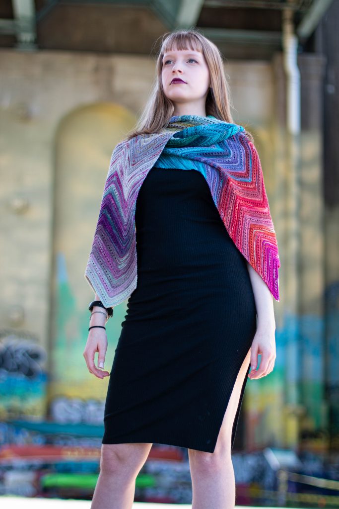 A gorgous multicoloured shawl knit with SpaceCadet Mini-Skeins, worn by a model standing under one of Pittsburgh's bridges