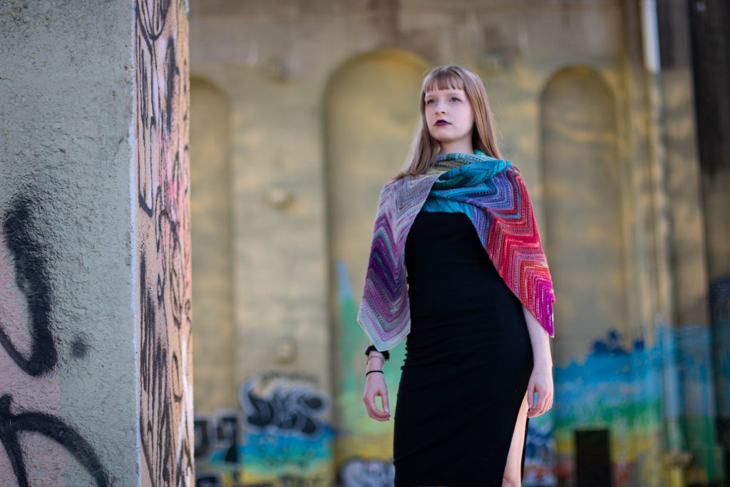 A gorgous multicoloured shawl knit with SpaceCadet Mini-Skeins, worn by a model standing under one of Pittsburgh's bridges